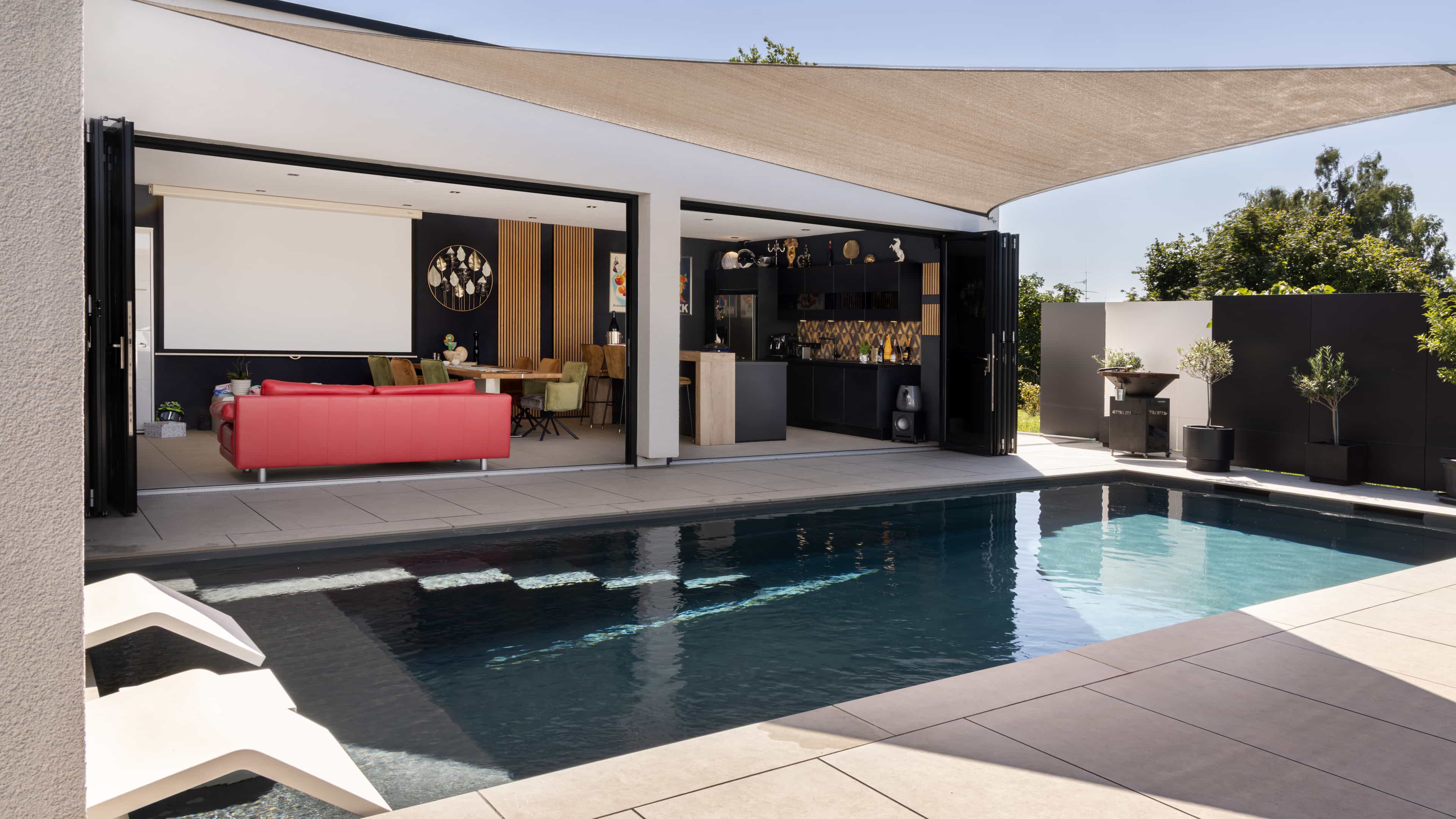 Pool mit Sonnensegel vor dem offenen Wohnbereich mit roter Couch, Außenansicht Familienhaus Eder von Haas