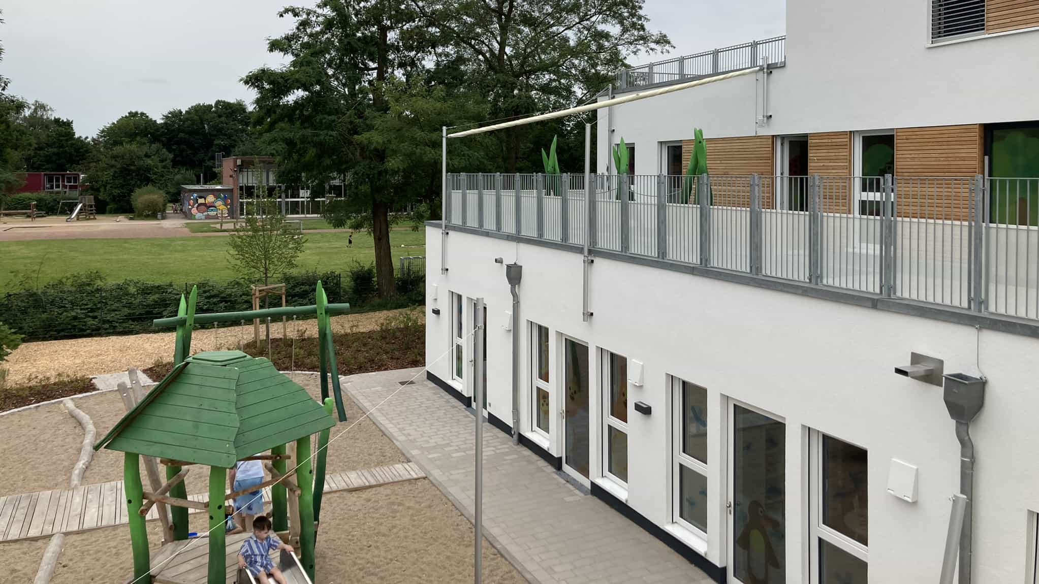 Außenansicht der zweigeschossigen Kita KD1 mit Dachterrasse und Spielhaus im Vordergrund