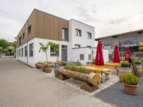 Außenansicht der Weinwirtschaft Burgblick mit Biergarten, Holzbänken und roten Sonnenschirmen vor dem Gebäude