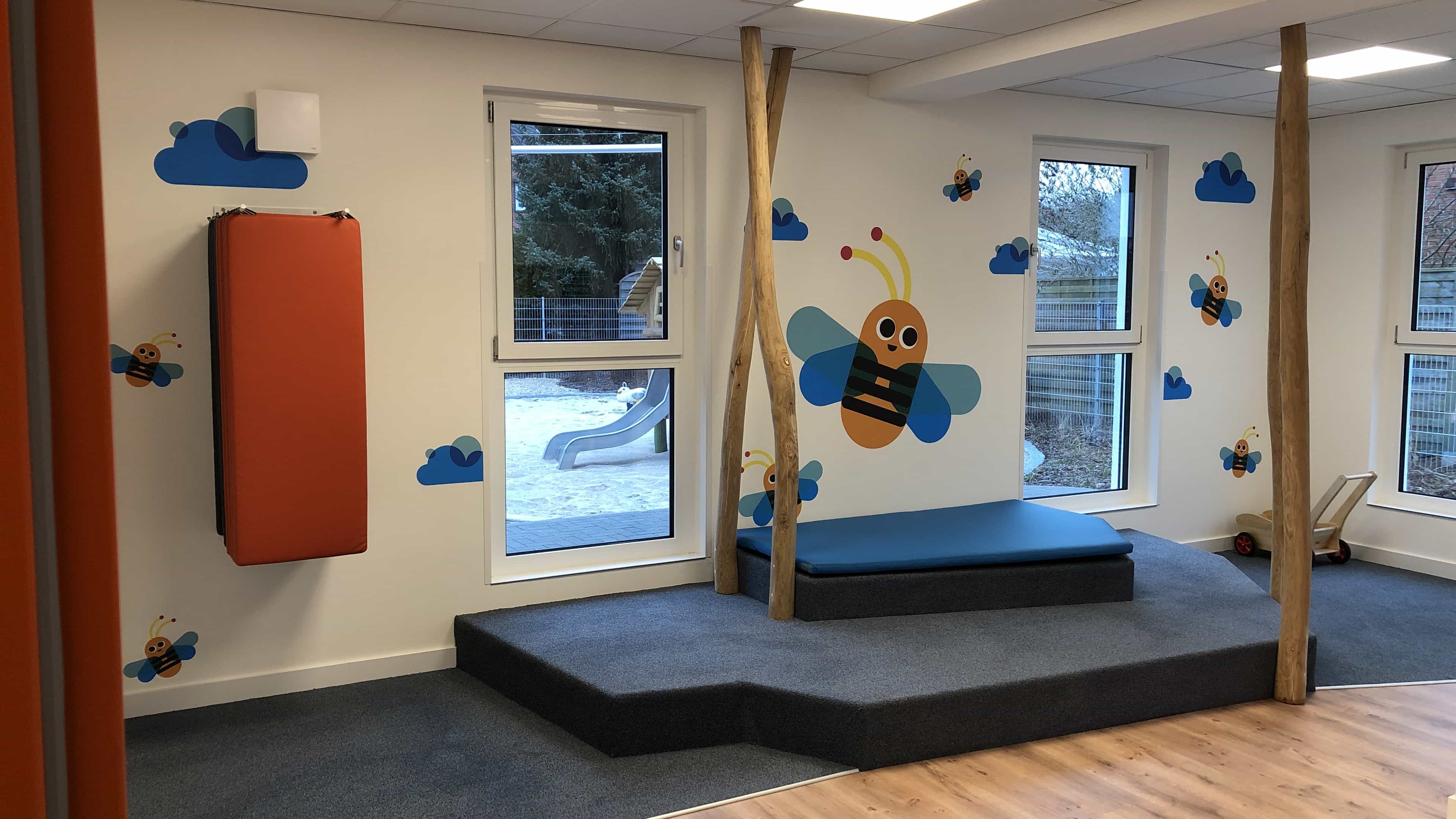 Gruppenraum der Kita KD3 mit Spielpodest, Holzstämmen und Bienen-Wandbild