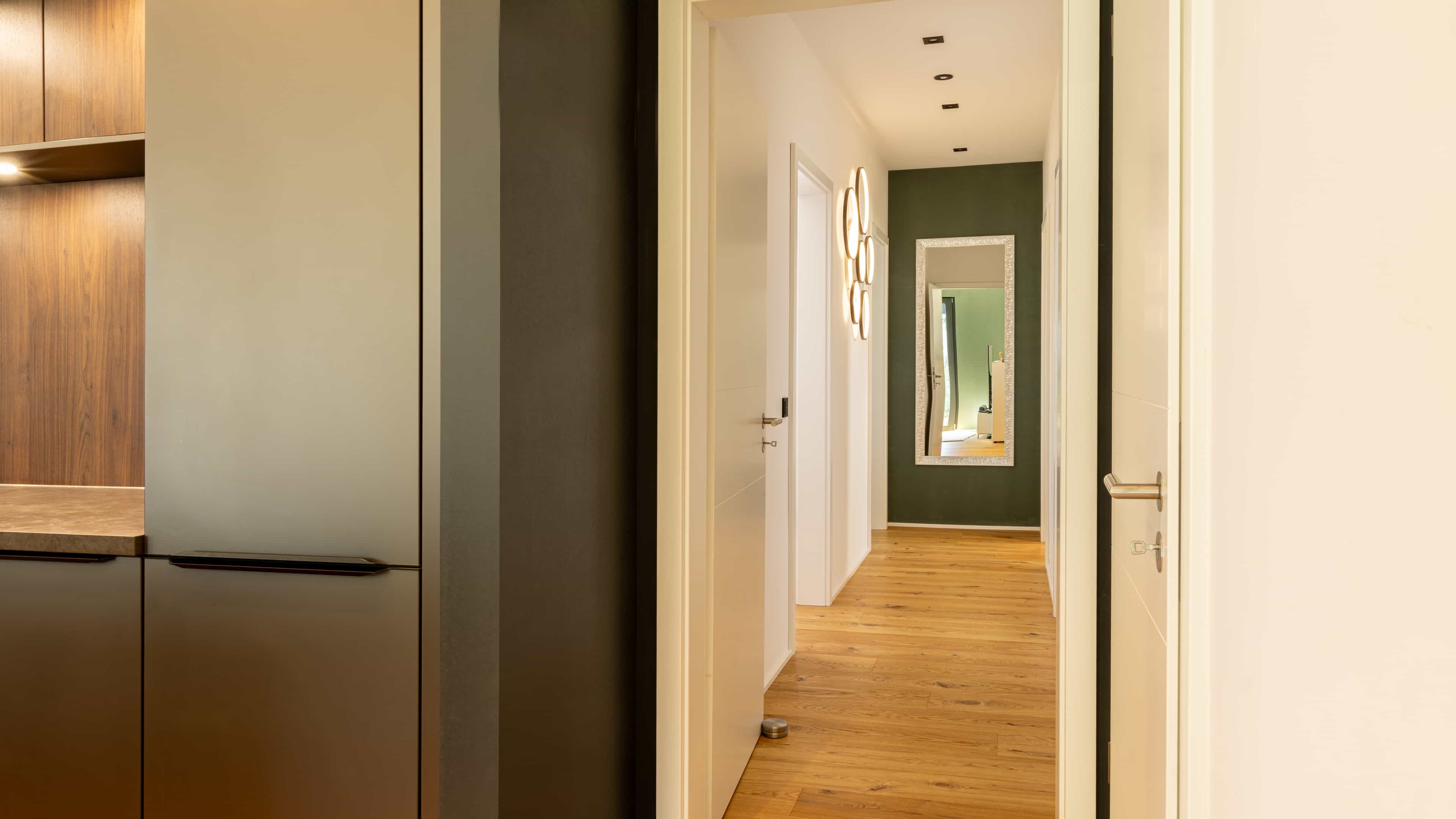 Flur mit Holzdielen, grüner Wand und Spiegel im Bungalow der Familie Eder von Haas Fertigbau