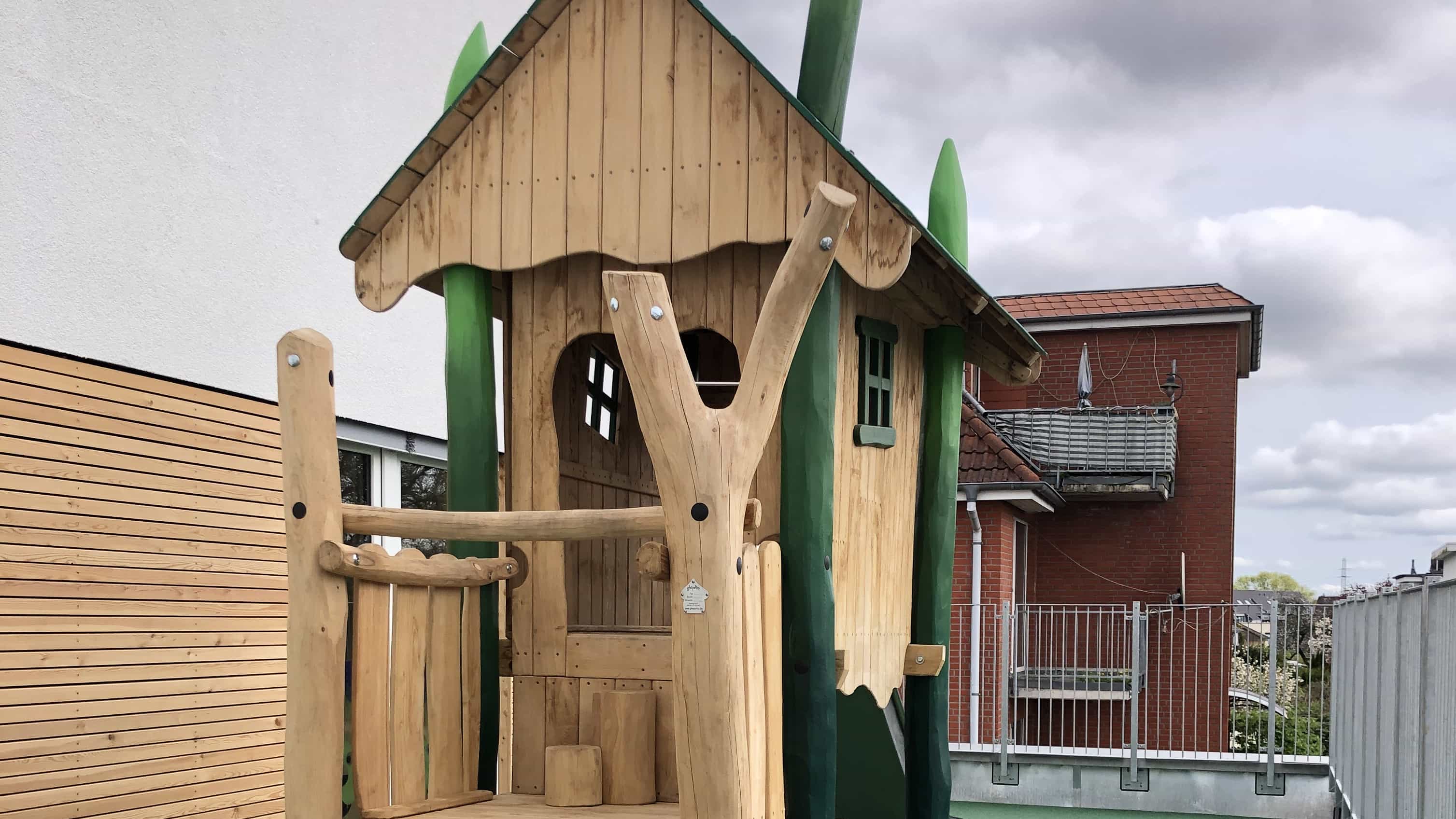 Holzspielhaus auf dem Außengelände der Kita KD1 mit Holzfassade im Hintergrund
