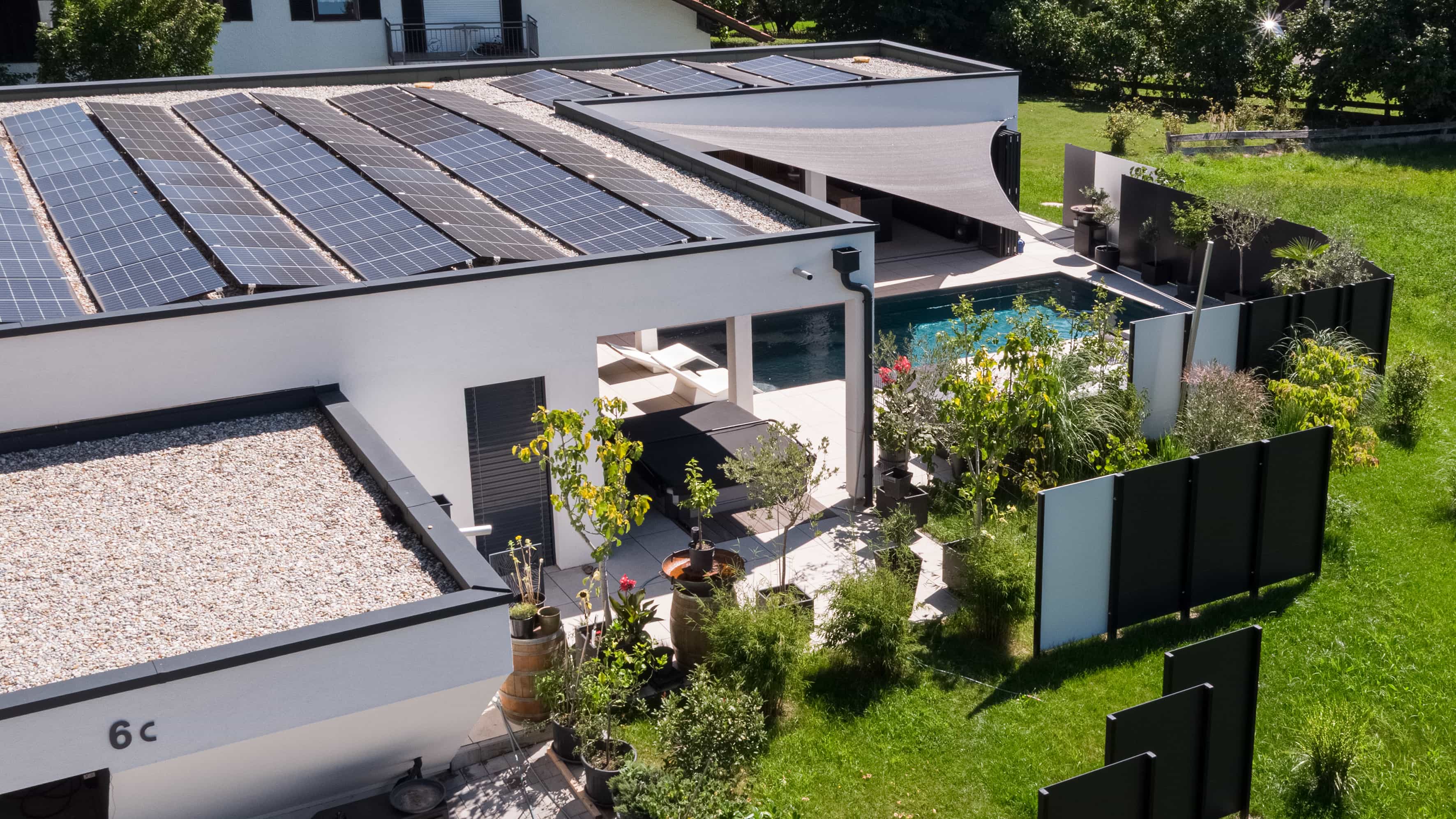 Luftaufnahme des Flachdach-Bungalows der Familie Eder mit Photovoltaikanlage, Pool und Garten