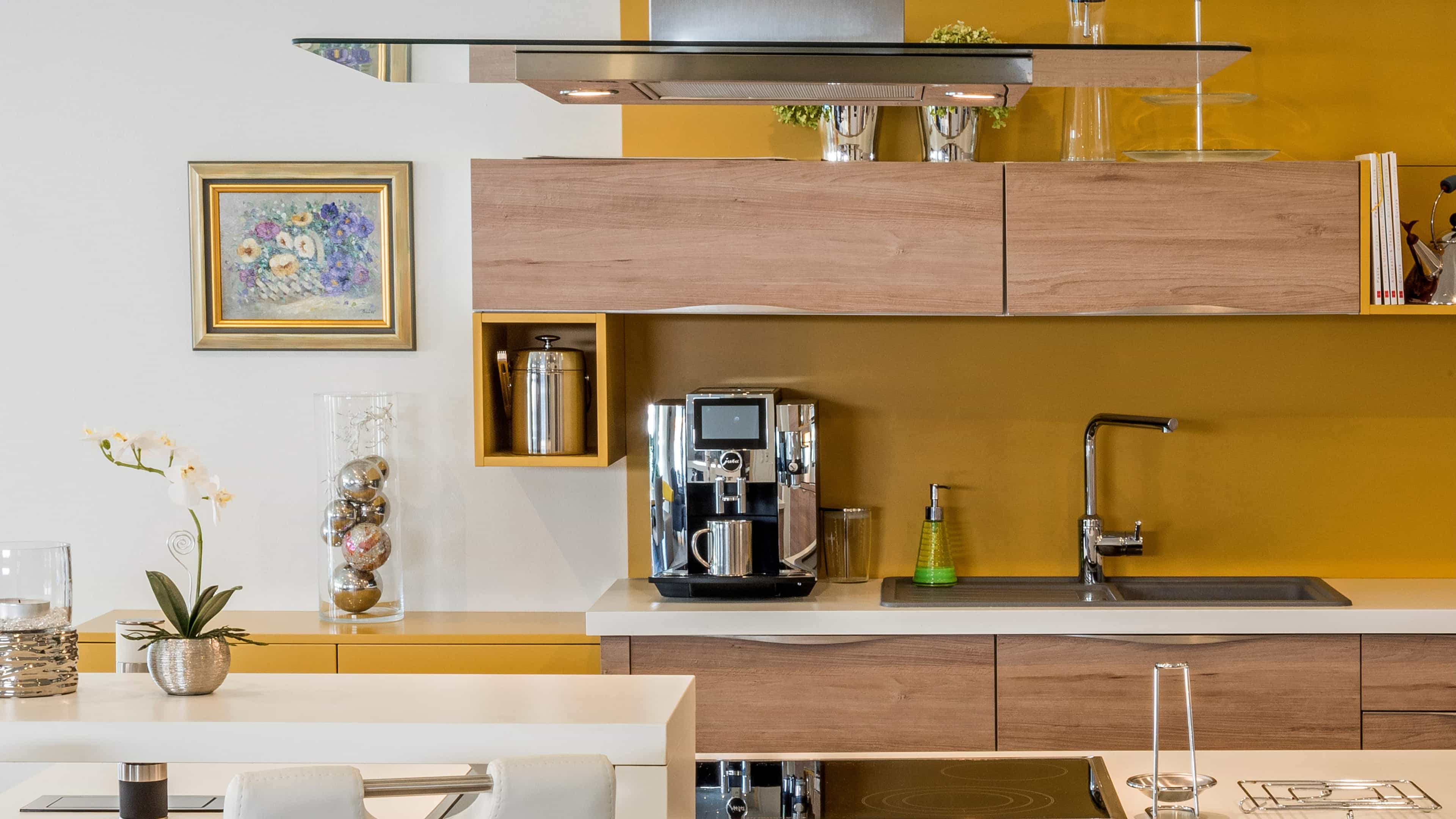 Moderne Küche mit gelben Wänden, Holzschränken, Kaffeemaschine, Spüle, Orchidee und Wandbild im Hintergrund.