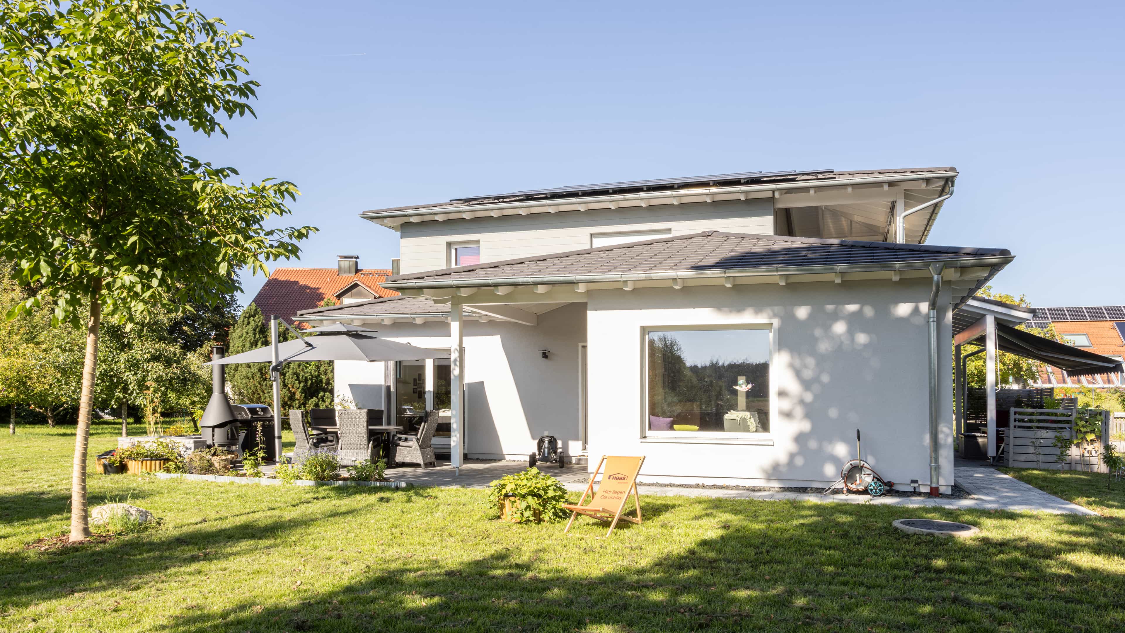 Gartenansicht des Familienhauses Lampl mit weißer Fassade, Staffelgeschoss und überdachter Terrasse