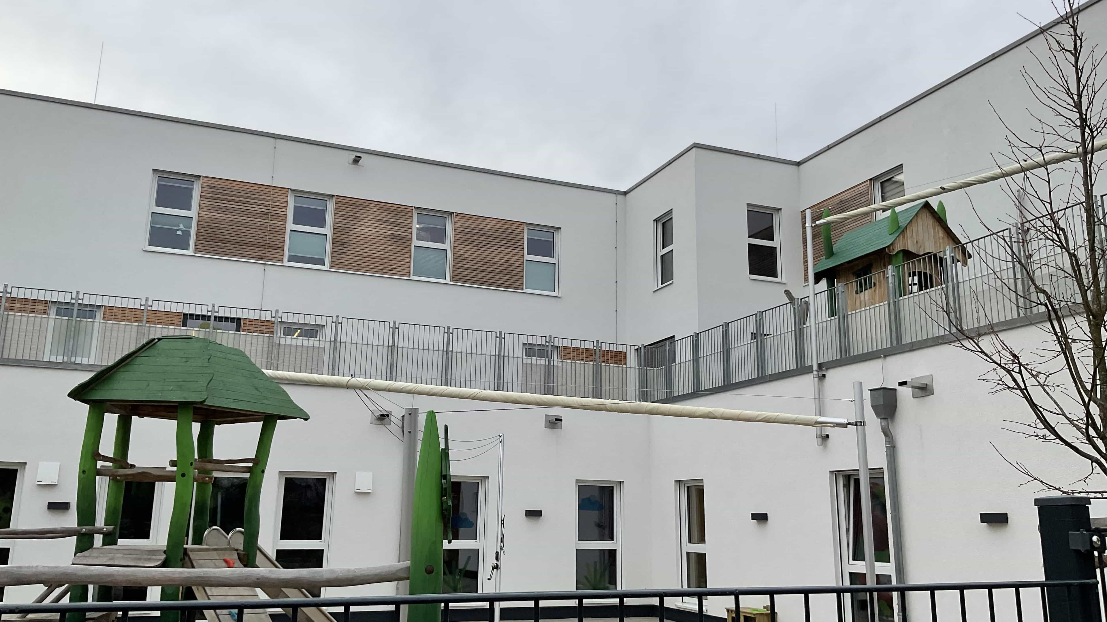 Gebäudeecke der Kita KD1 mit Dachterrassen-Geländer und Spielgerät im Vordergrund