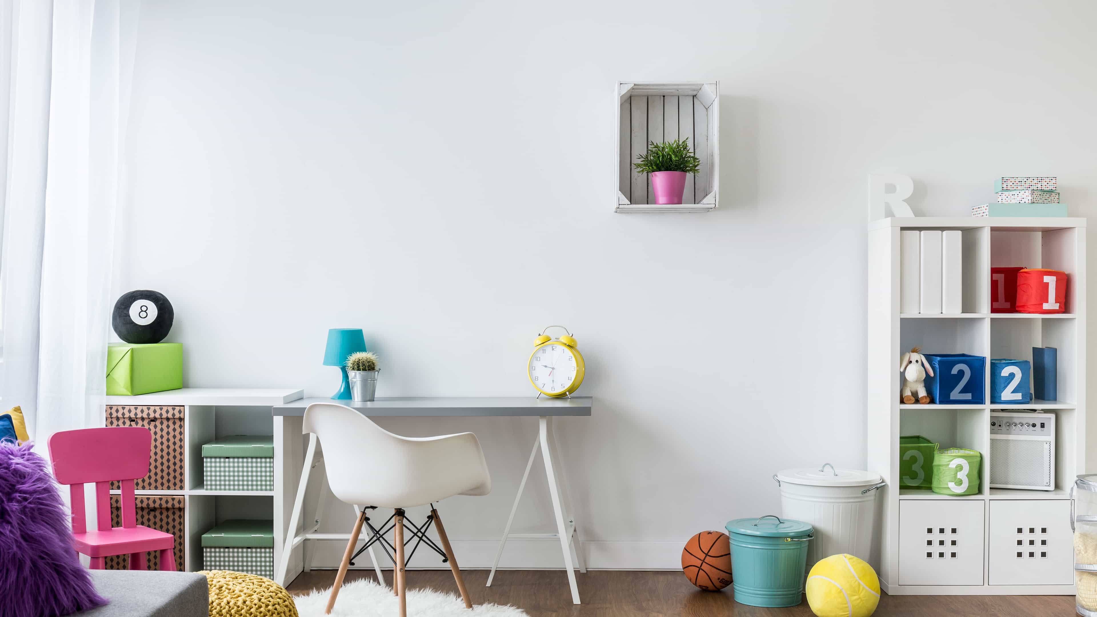 Helles Kinderzimmer mit Schreibtisch, Stuhl und Regal, dekoriert mit leuchtenden Farben, Spielzeug und Büchern.