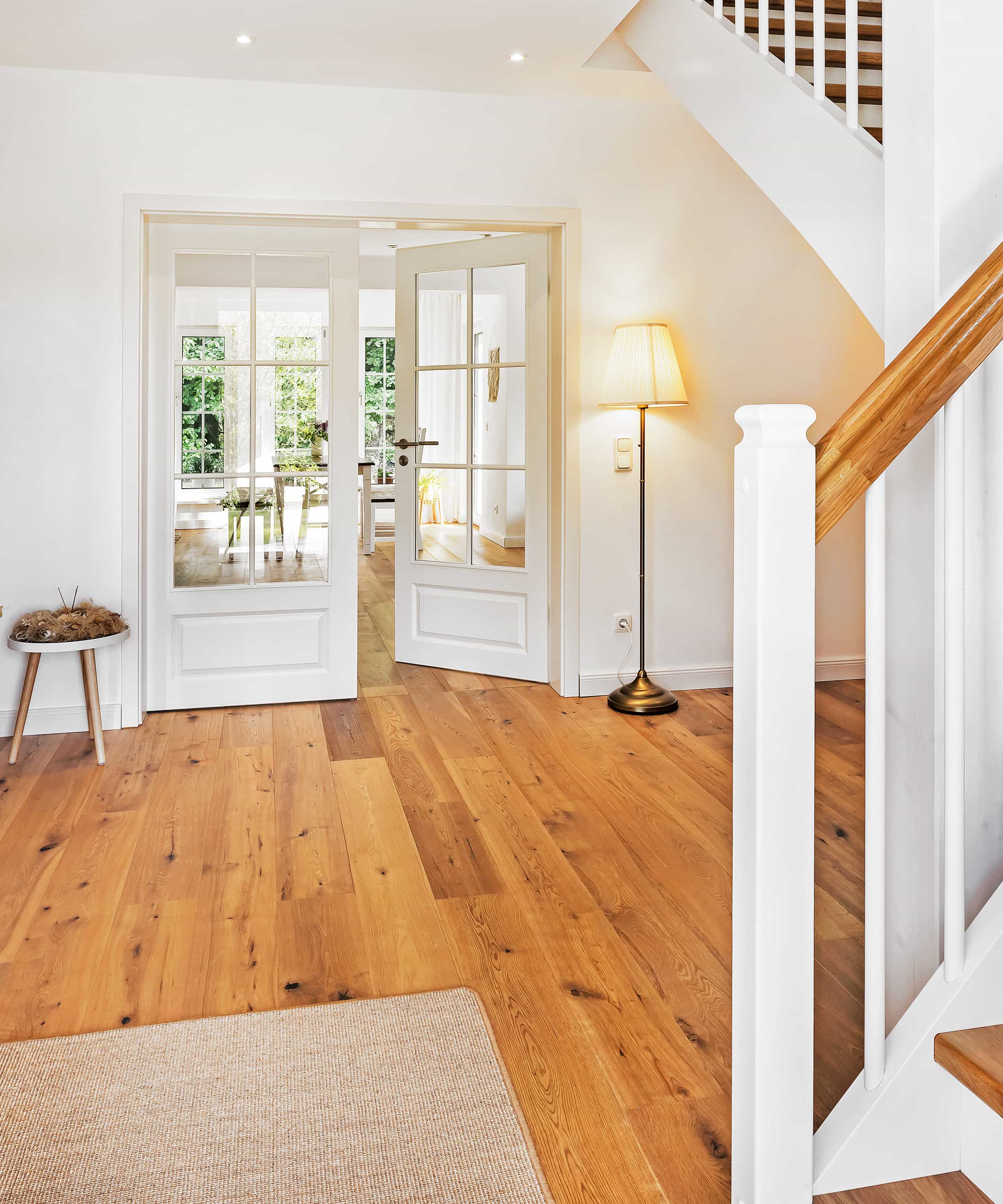 Helles, einladendes Foyer mit Holztreppe, geöffneten Doppeltüren und natürlichem Lichteinfall im Hintergrund.