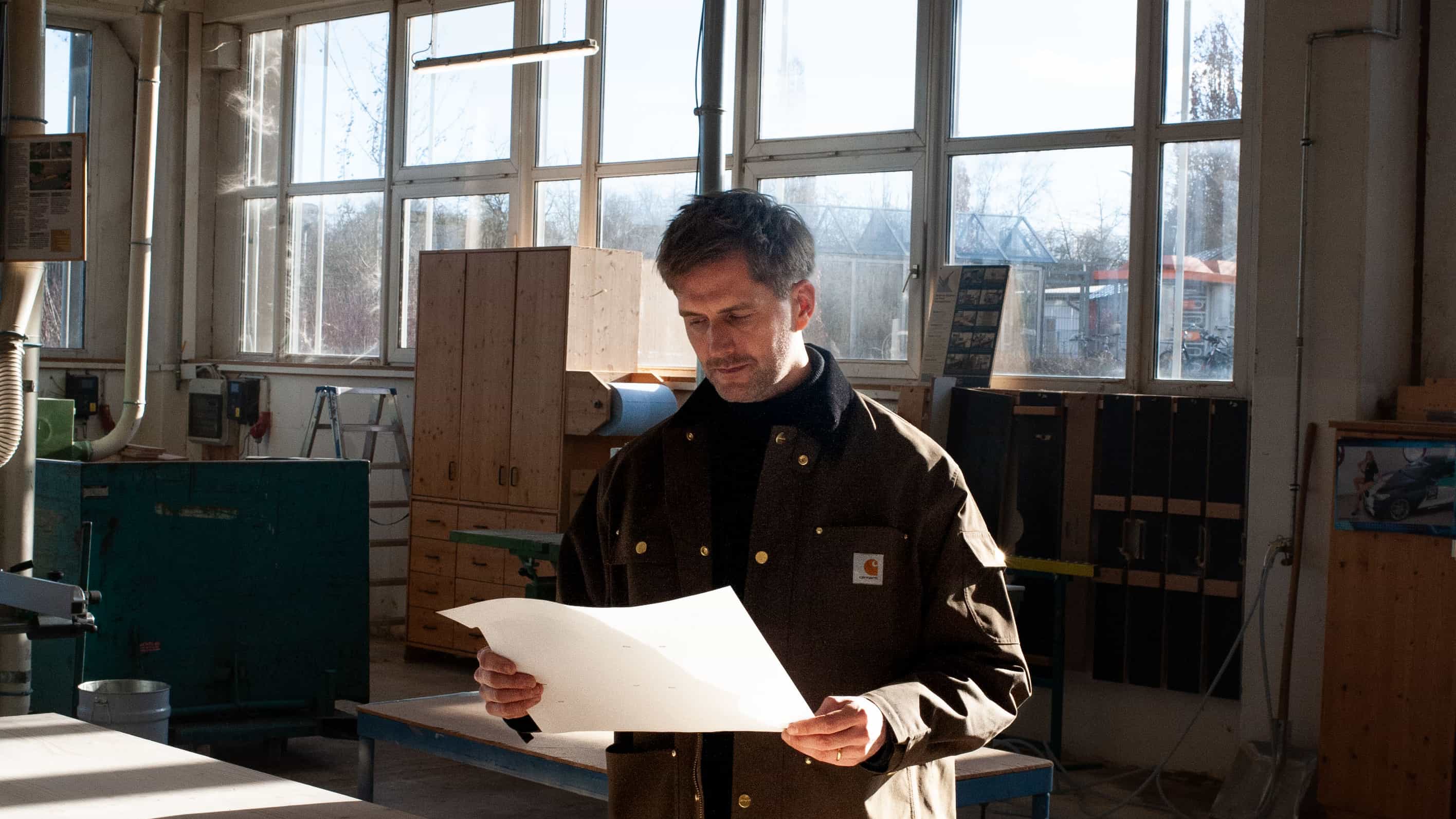 Architekt prüft einen Bauplan in der Holzwerkstatt, Lookbook Architektenhäuser Haas x Sigurd Larsen