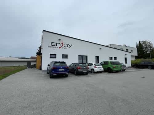 Neubau des Fitnesscenters Enjoy Fitness mit weißer Fassade, Logo und Parkplatz von Haas Gewerbebau
