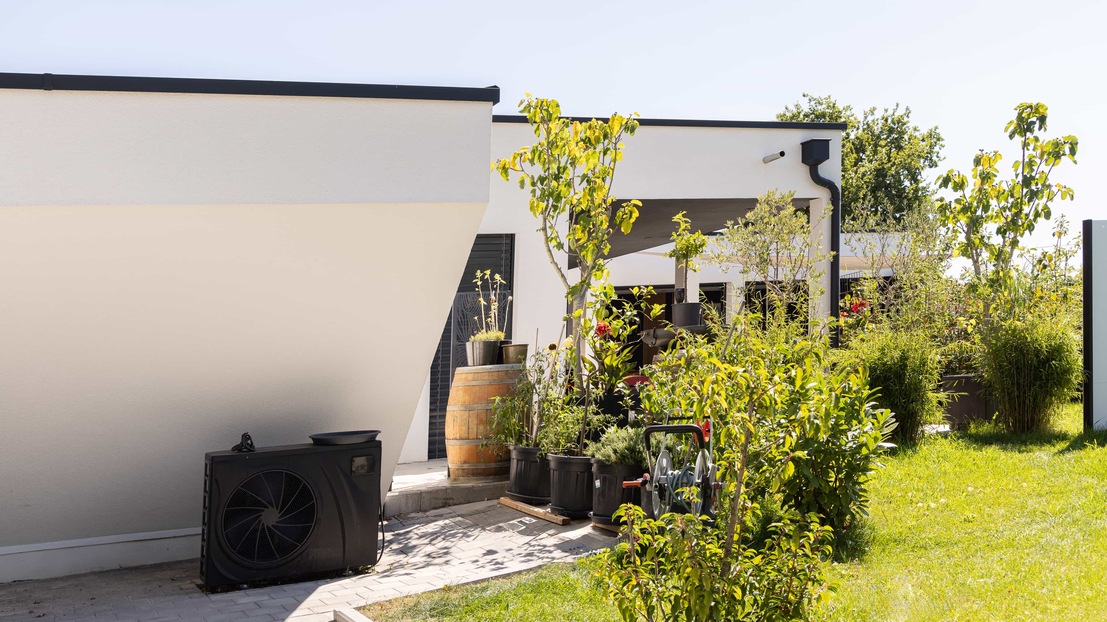 Wärmepumpen-Außeneinheit an der weißen Fassade des Bungalows der Familie Eder mit Garten