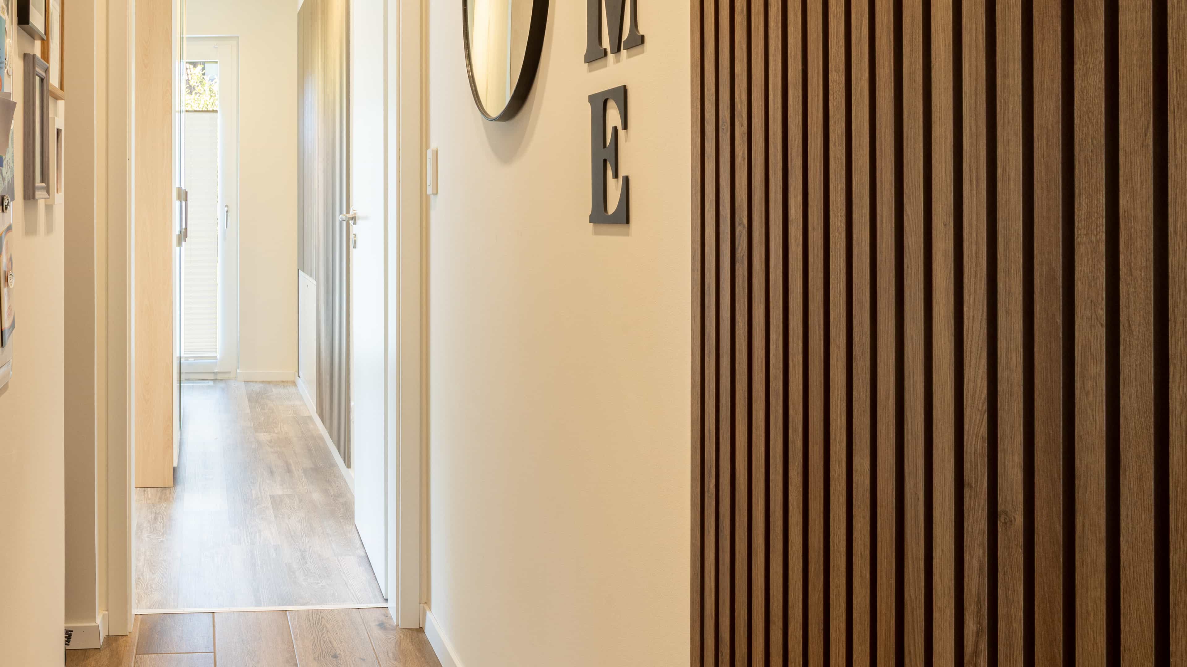 Flur mit Holzlamellenwand und rundem Spiegel im Familienhaus Lampl von Haas Fertigbau