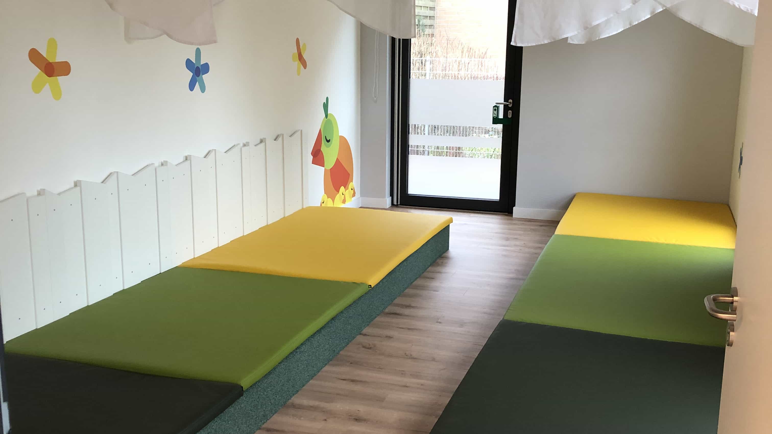 Ruhebereich der Kita KD3 mit gelb-grünen Matten und Vogel-Wandmalerei