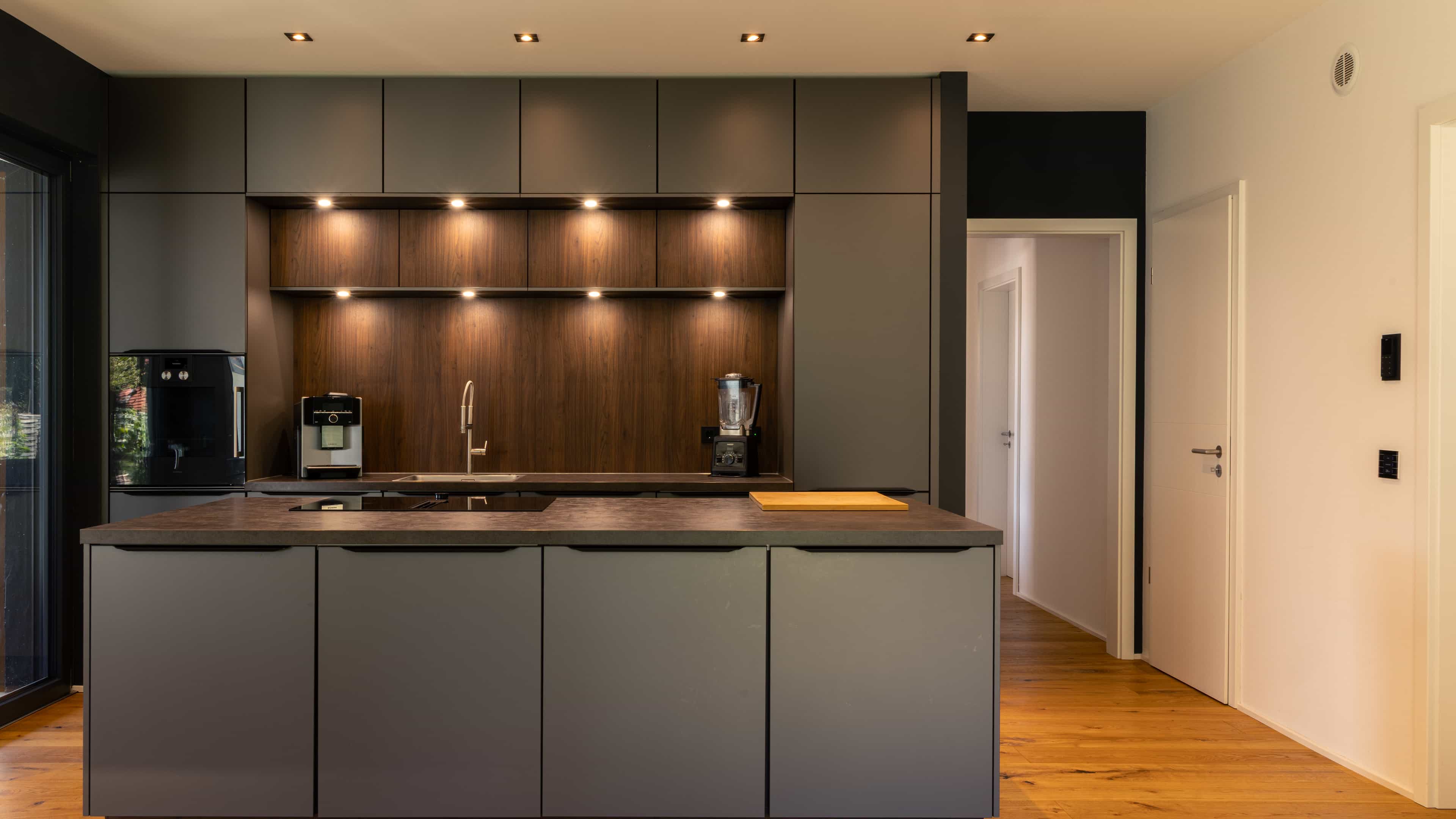 Küche mit anthrazitfarbenen Fronten, Kochinsel und Holzrückwand im Familienhaus Eder von Haas