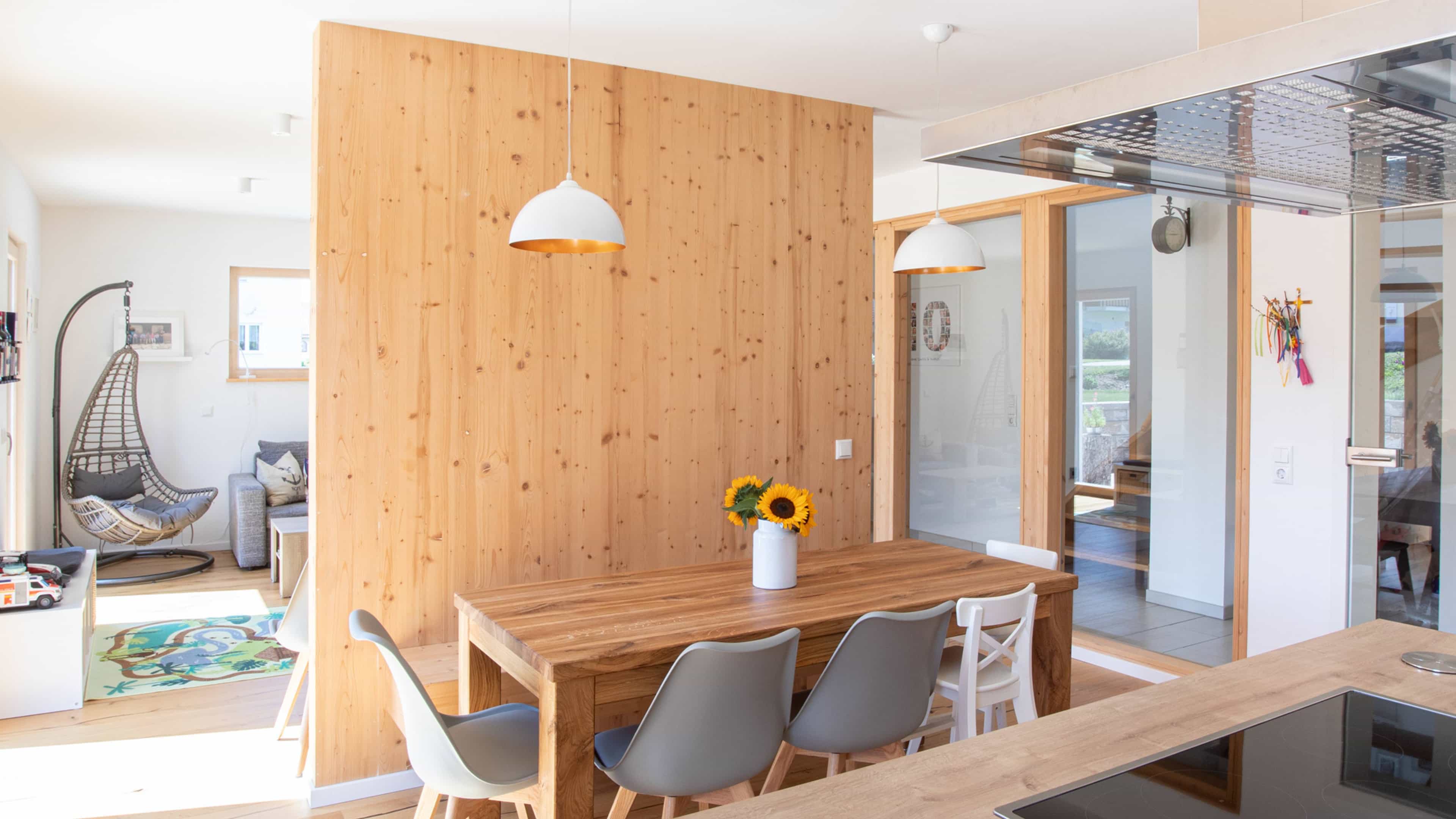 Essbereich aus Holz mit Esstisch und gemischten Stühlen, Sonnenblumen in Vase, hängender Sessel im Hintergrund.