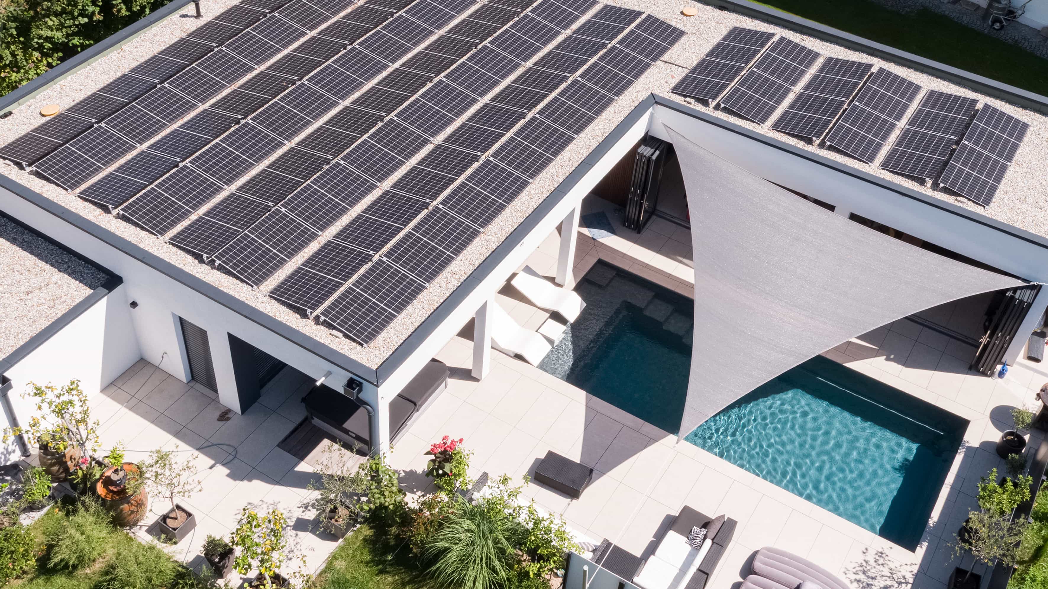 Luftaufnahme von oben auf das Photovoltaikdach, Sonnensegel und Pool des Familienhauses Eder