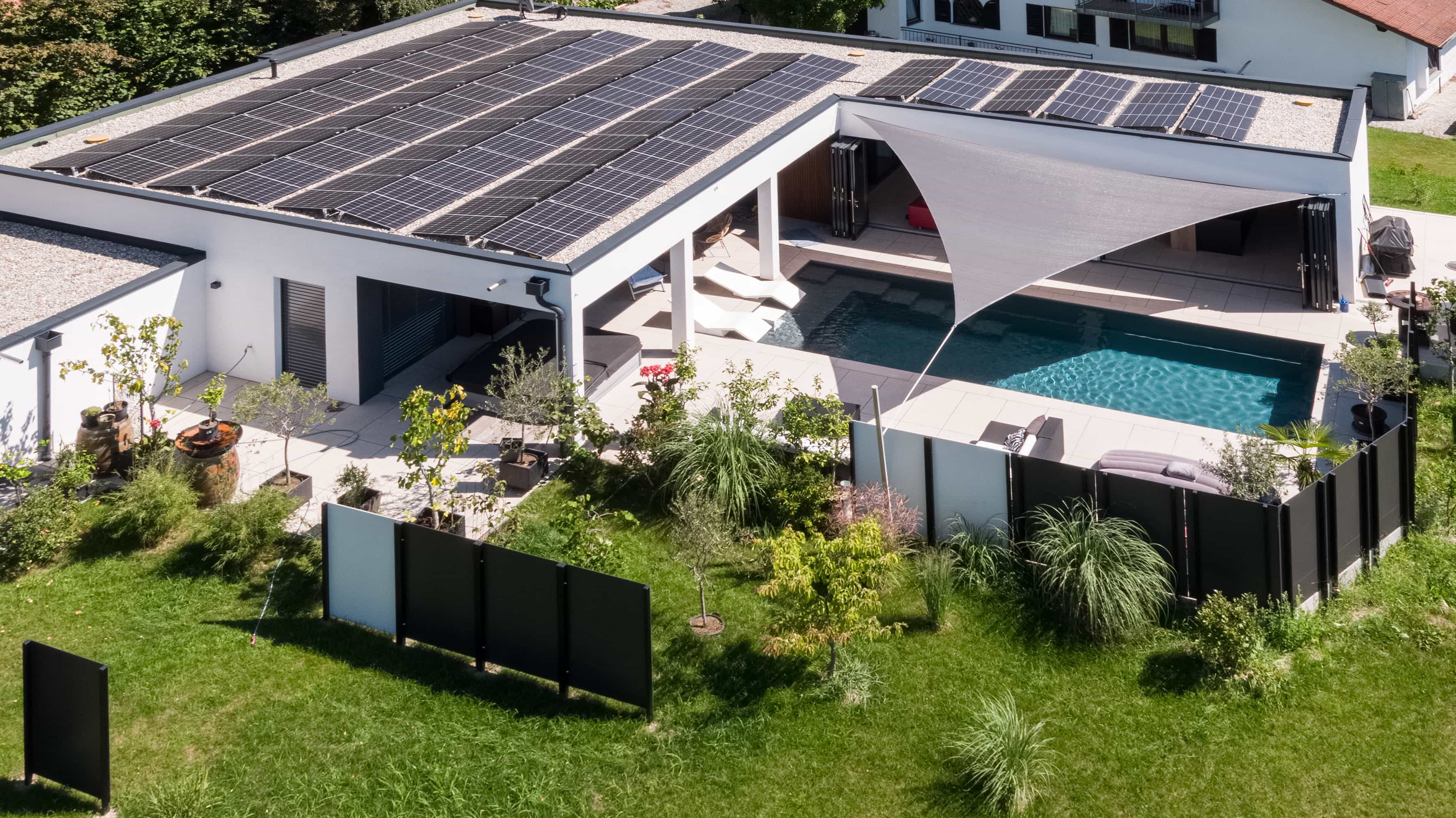 Schräge Luftaufnahme des Bungalows der Familie Eder mit Photovoltaik, Pool und Garten mit Sichtschutz