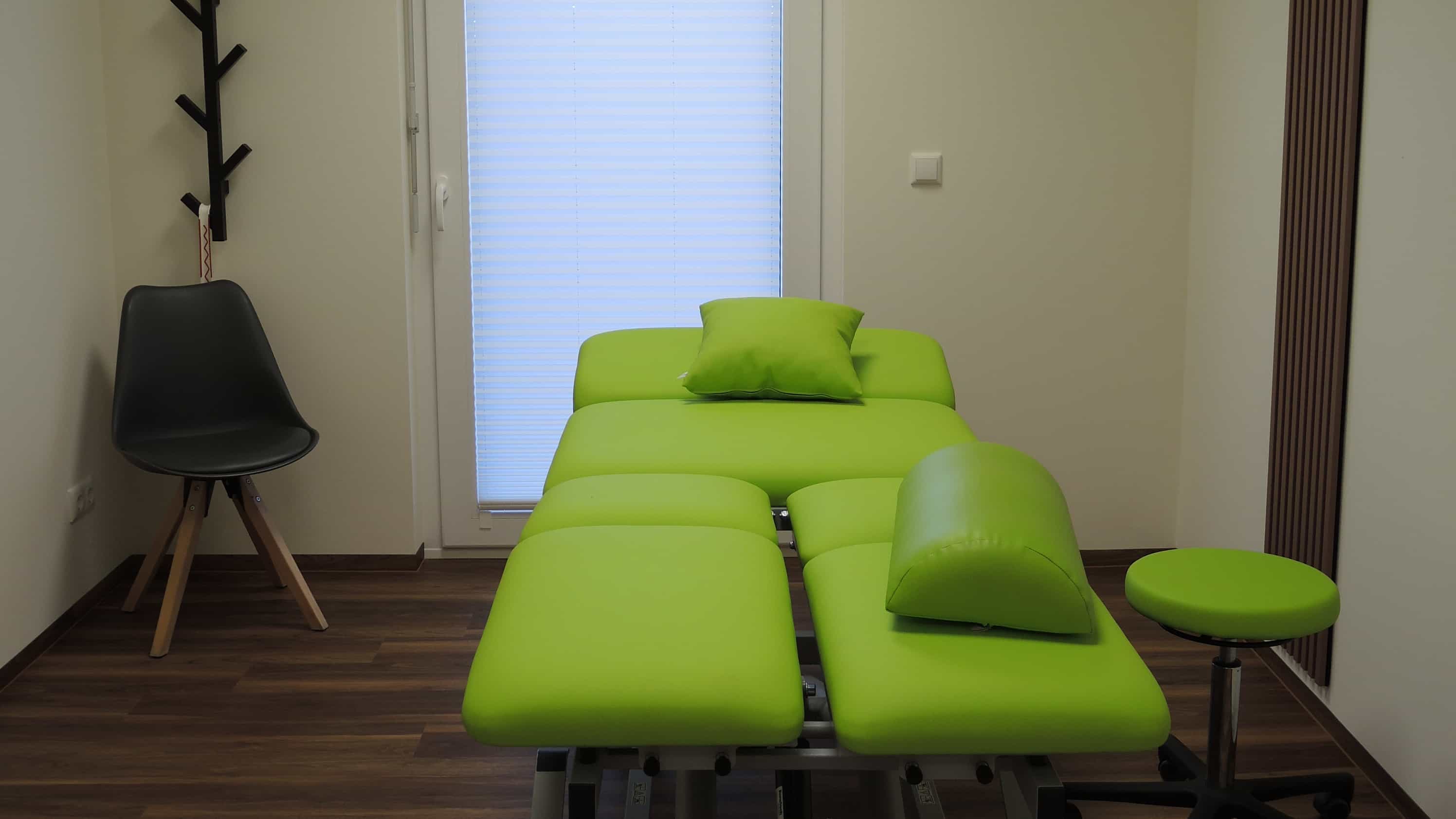 Behandlungsraum der Praxis Ellrich mit grüner Therapieliege, Hocker und Garderobe