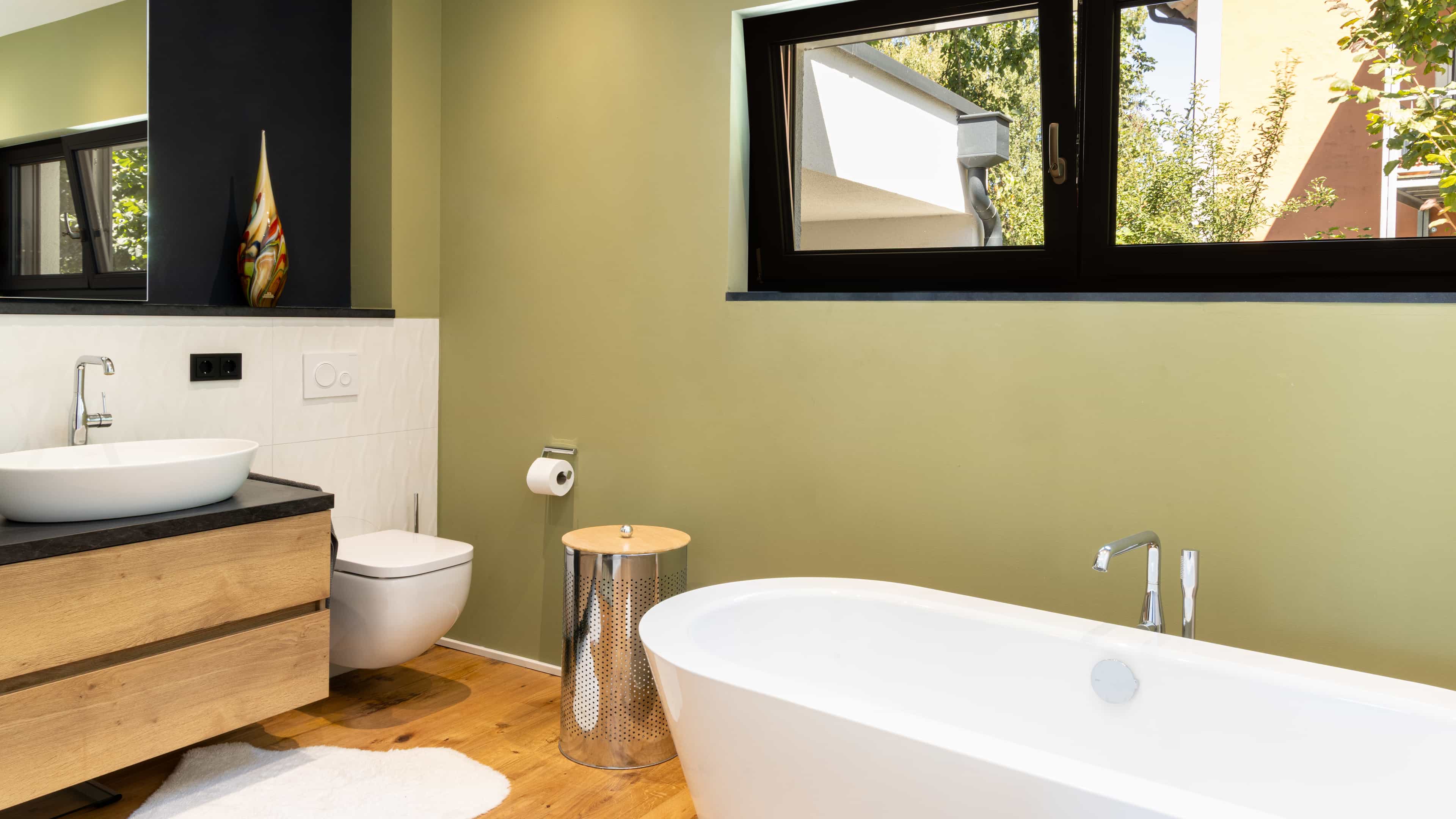 Badezimmer mit grüner Wand, freistehender Wanne und Holzwaschtisch im Familienhaus Eder von Haas