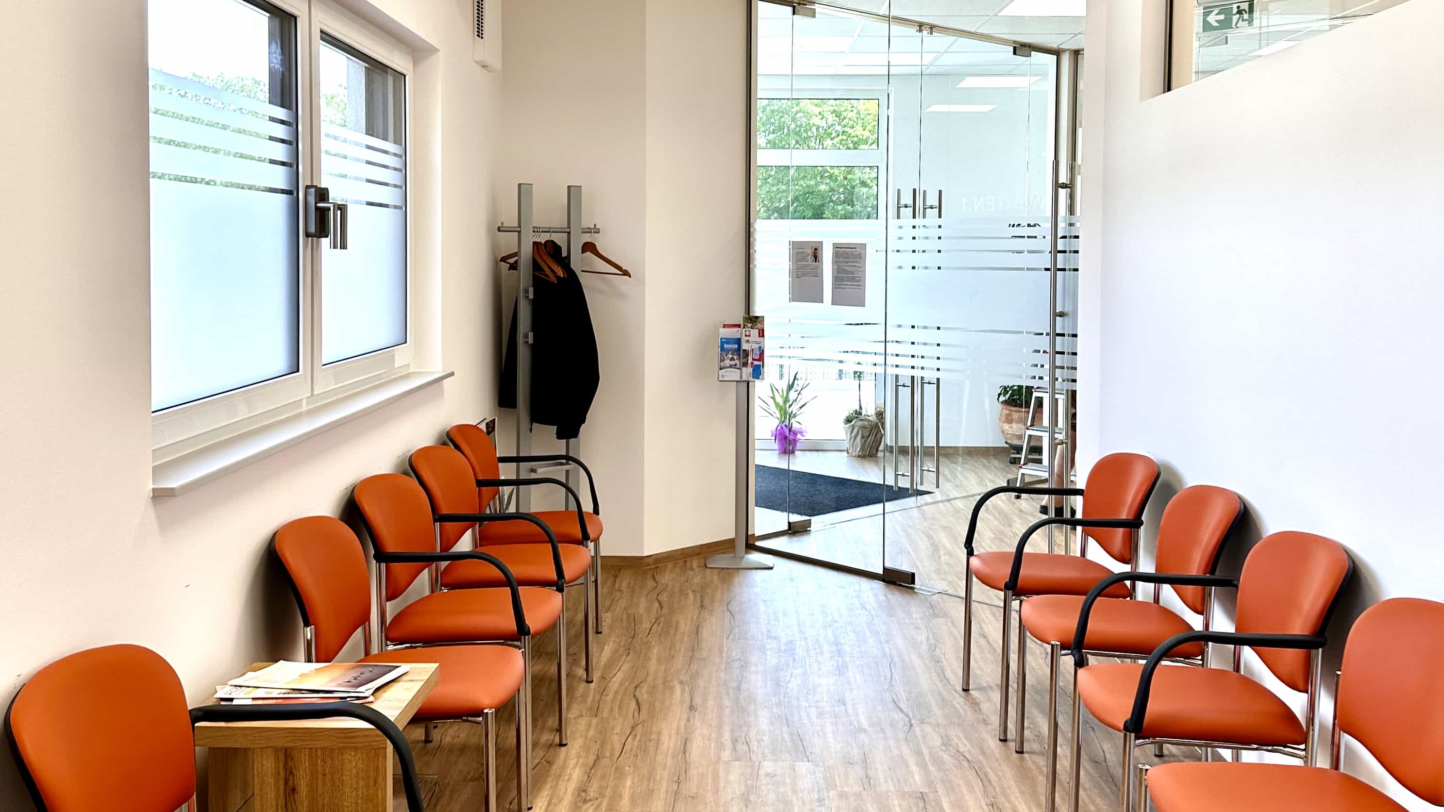 Wartebereich der Praxis Balzer mit orangen Stühlen und Blick zum Eingang