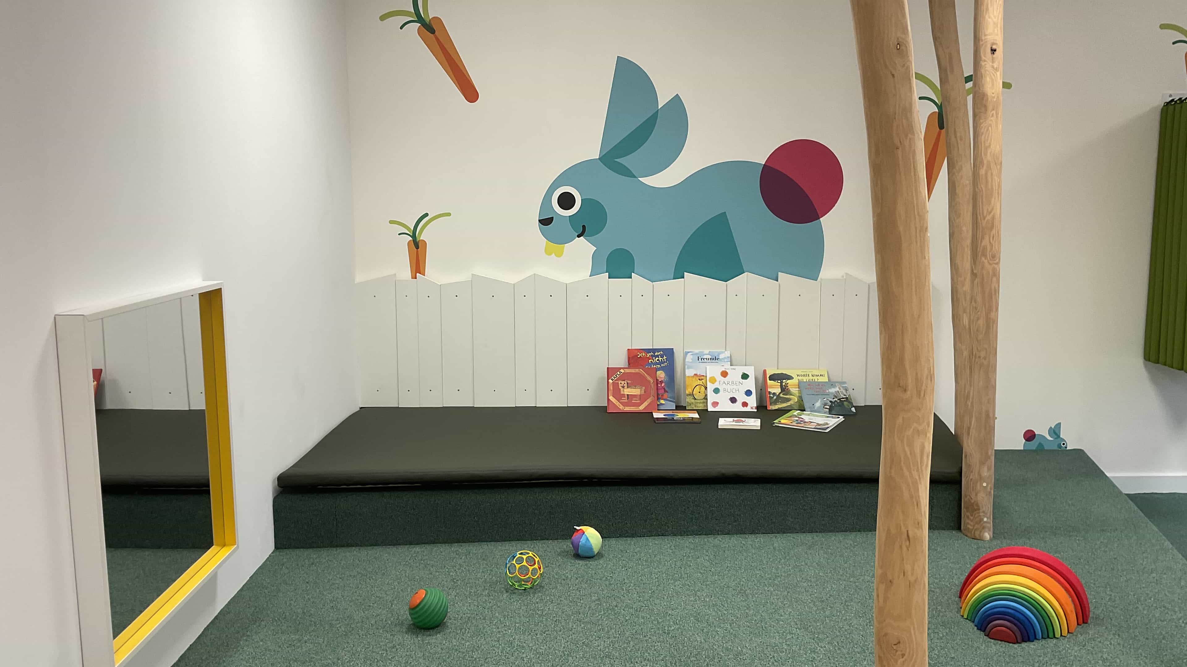Spielpodest mit Spiegel, Hasen-Wandbild und Holzstämmen in der Kita KD3