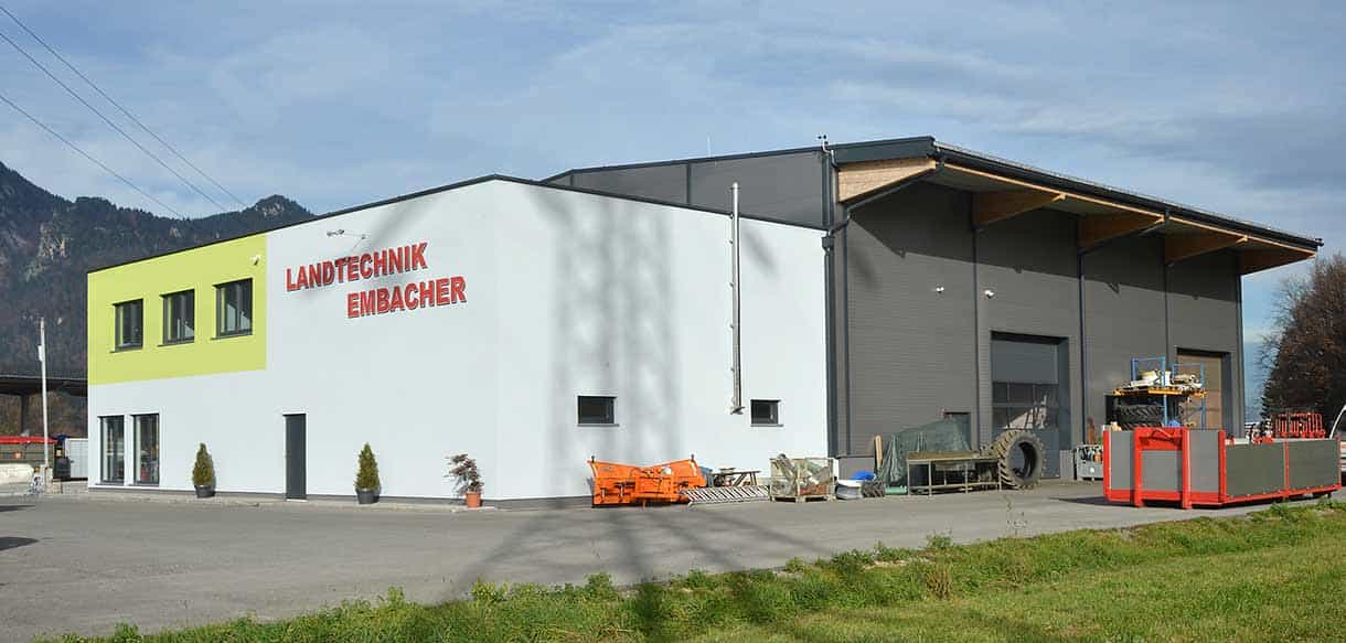 Seitenansicht der Halle von Landtechnik Embacher mit Schriftzug vor Bergkulisse