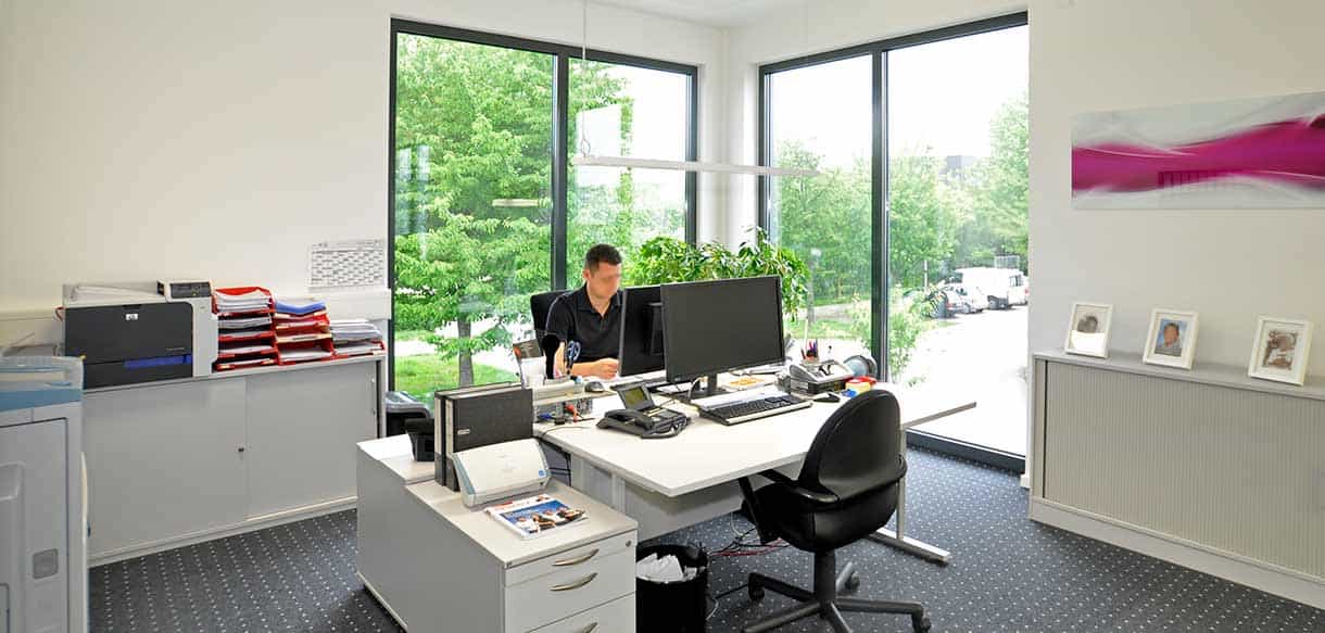 Büro mit Mitarbeiter am Schreibtisch und großer Fensterfront bei RM Bodenbeläge