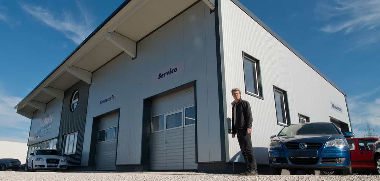 Seitenansicht der Kfz-Werkstatt von Autopark Windern mit Sektionaltoren, Mitarbeiter vor dem Gebäude