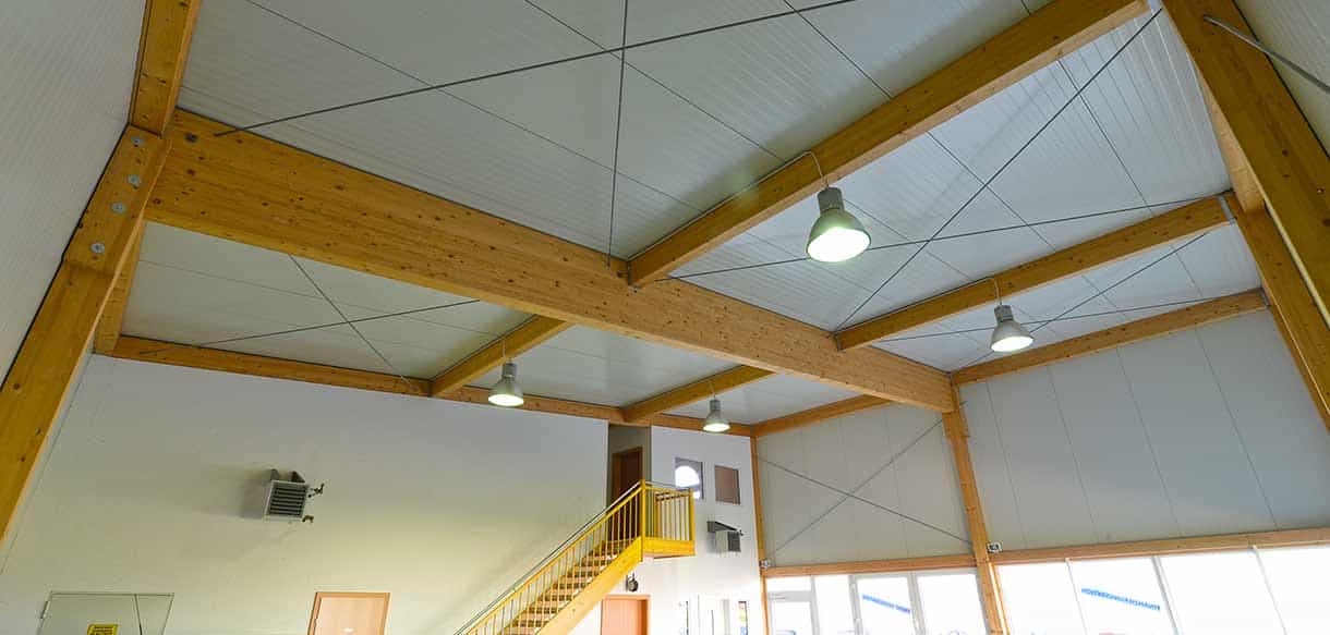 Holzbinderdecke mit Industrieleuchten und gelbem Galeriegeländer in der Werkstatt von Autopark Windern