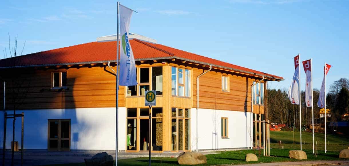 Verkaufsgebäude von Bergzeit Outdoor in Holzkirchen mit Holzfassade, Ziegeldach und Fahnenmasten von Haas Gewerbebau