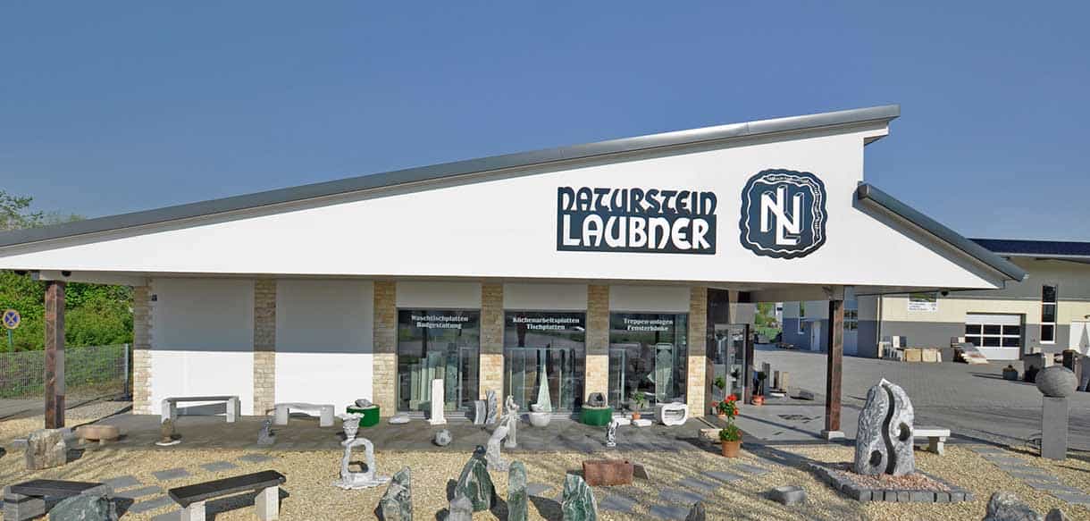 Frontansicht des Ausstellungs- und Verkaufsgebäudes von Naturstein Laubner mit Schriftzug und Natursteinen davor