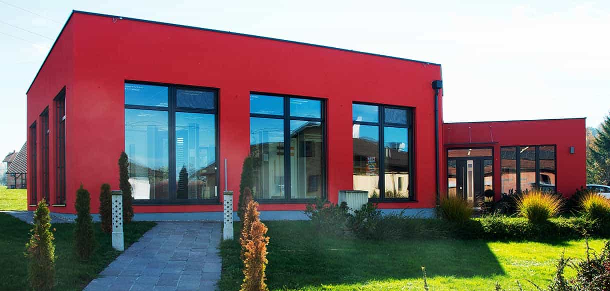 Roter Flachdach-Neubau mit großer Glasfront und Eingangsweg, Ausstellungsraum von Vorhauer Fenstersanierung und Haustüren, Haas Gewerbebau