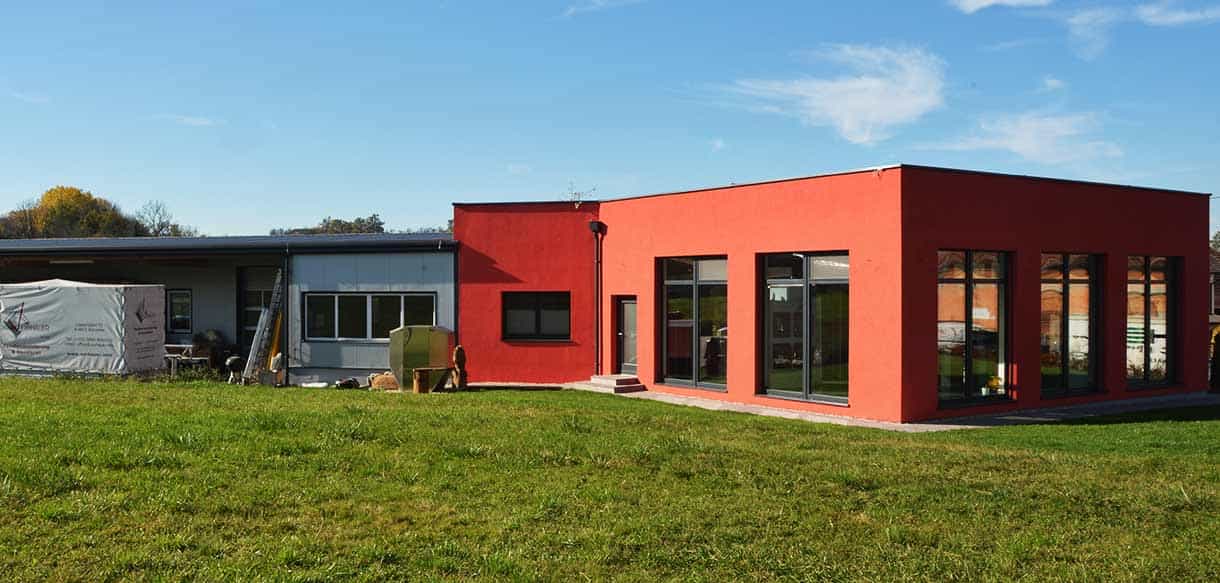 Rückseite des roten Büro- und Ausstellungsgebäudes von Vorhauer mit Rasenfläche und Fensterfront, Haas Gewerbebau