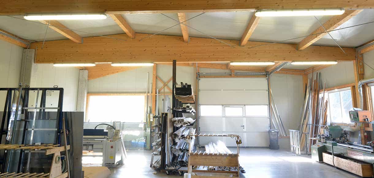 Produktionshalle von Vorhauer mit Holzleimbindern, Fensterprofilen und Maschinen unter Oberlichtern, Innenansicht
