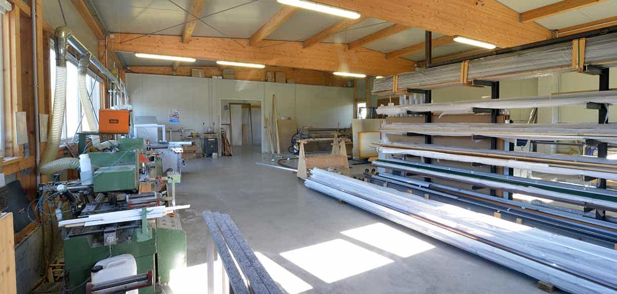 Maschinenbereich in der Produktionshalle von Vorhauer mit gelagerten Fensterprofilen und Holzdachträgern