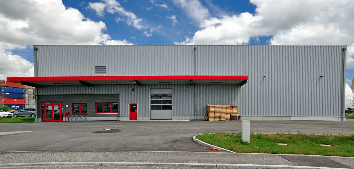 Frontansicht der Lagerhalle von Adler Lacke in Dornstadt mit roter Vordachkante und Hallentor