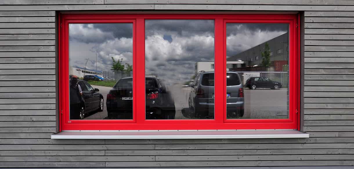 Rotes Fensterelement in der grauen Holzfassade der Lagerhalle von Adler Lacke, Fassadendetail