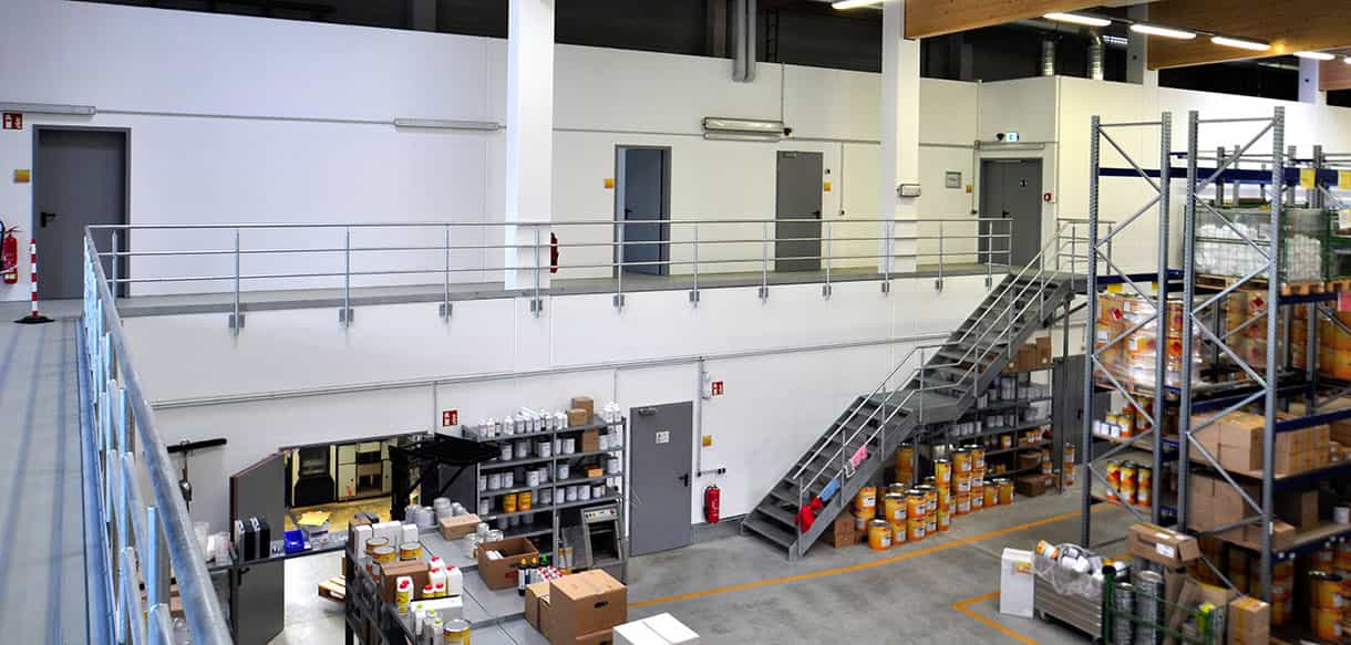 Blick von der Galerie ins Lacklager von Adler Lacke mit Hochregalen und Stahltreppe