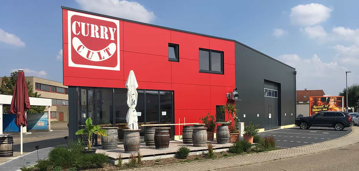 Imbiss mit Lagerhalle von Curry Cult mit roter Fassade und Weinfässern vor dem Eingang