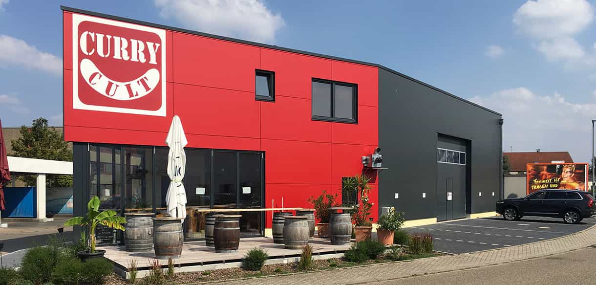 Curry Cult Imbiss und Lagerhalle von Haas Gewerbebau mit rotem Bürotrakt und grauer Hallenfassade