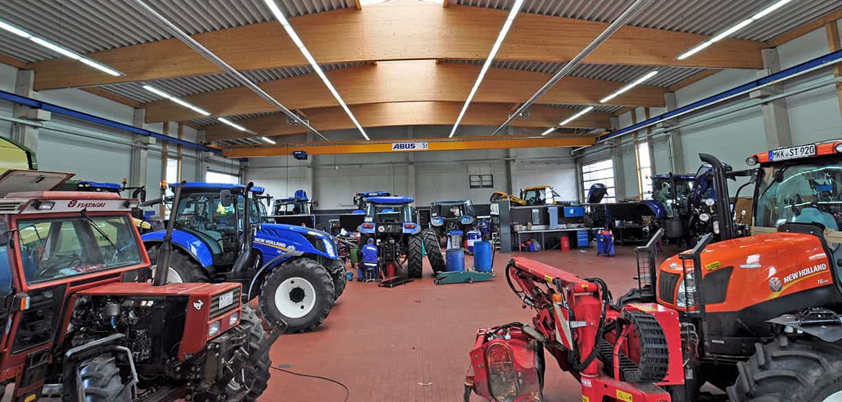 Werkstatt von Leinweber Landtechnik mit Traktoren, rotem Boden und Holzdach