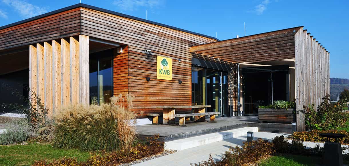 Eingangsbereich des KWB-Ausstellungsgebäudes mit Holzlamellen, Logo und Holzbank
