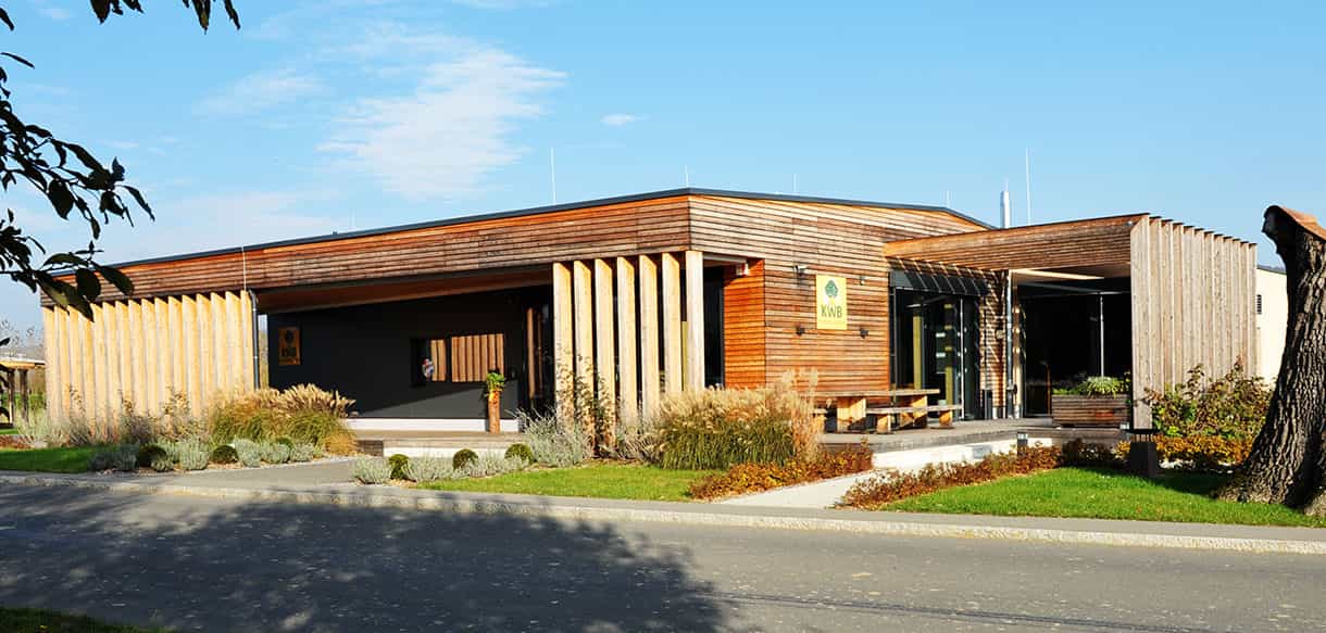 Straßenansicht des KWB-Ausstellungsgebäudes mit Holzfassade, Lamellen und Grünflächen