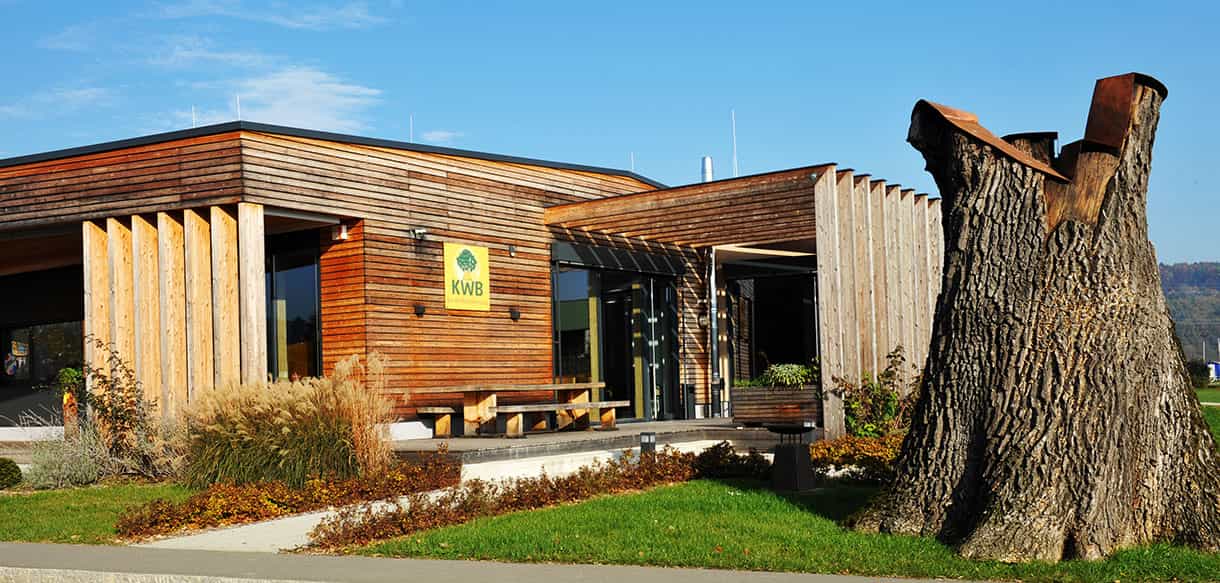 Baumstumpf-Skulptur vor dem KWB-Ausstellungsgebäude mit Holzfassade und Lamellen
