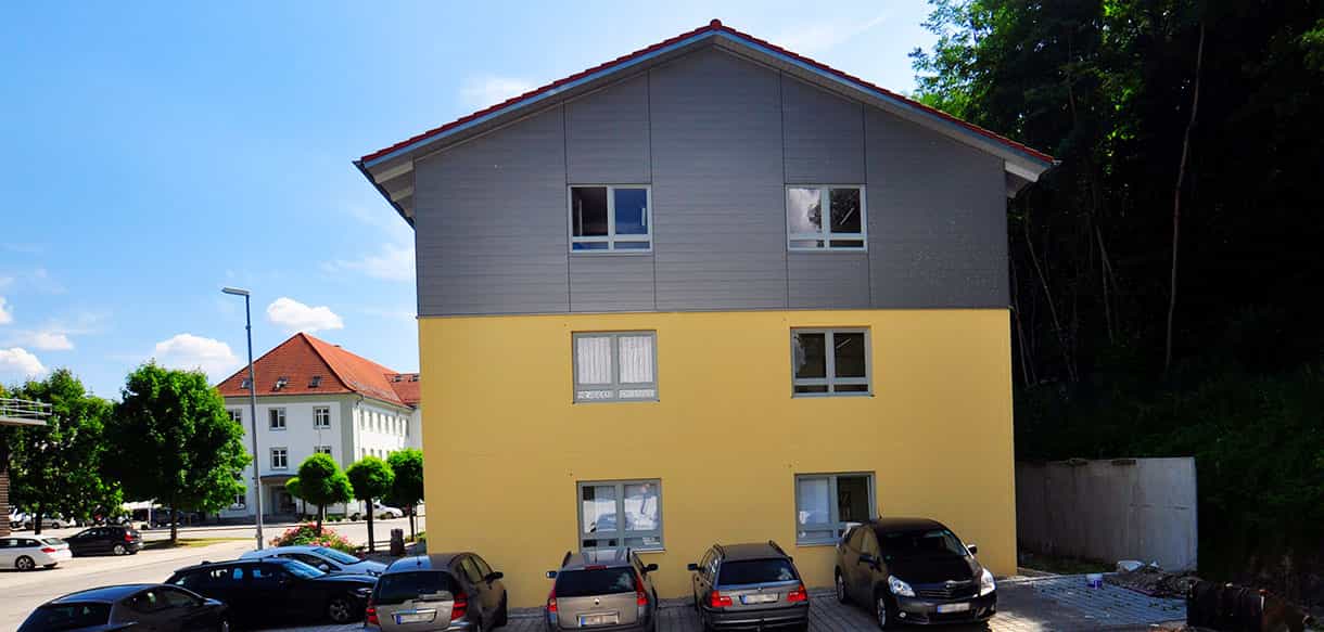 Giebelseite des Kaiser Gebäudes mit grauer Aufstockung und Parkplatz