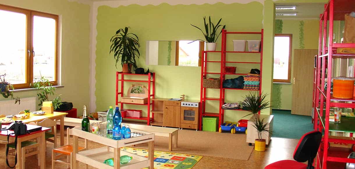 Gruppenraum des Kindergartens Sedmikráska mit grüner Wand, rotem Regal und Pflanzen