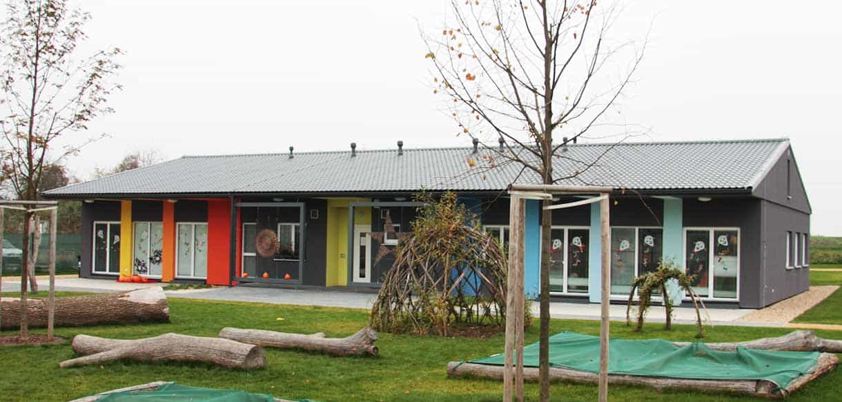 Eingeschossiger Kindergarten Přezletice mit grauer Fassade und bunten Fensterfeldern im Garten