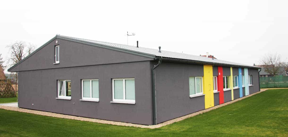 Giebelseite des Kindergartens Přezletice mit grauer Fassade und farbigen Fensterrahmen
