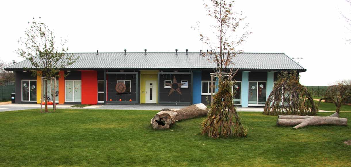 Gartenseite des Kindergartens Přezletice mit Wiese, Baumstämmen und Weidentipi