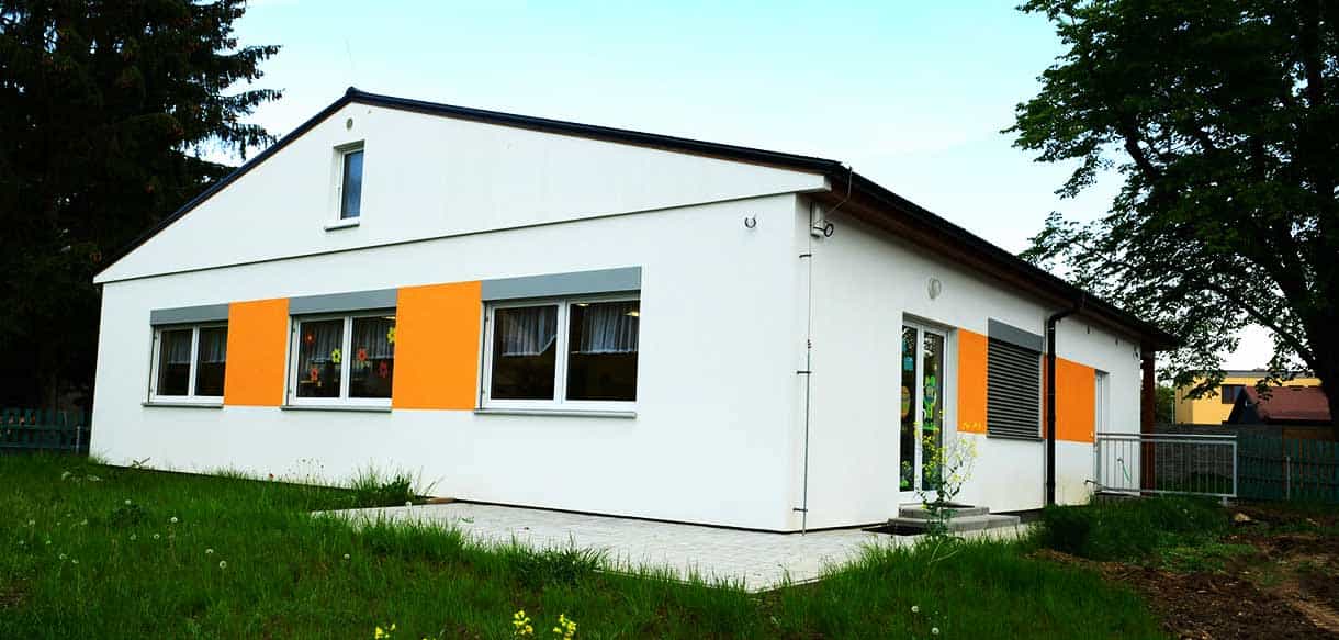 Rückseite des Kindergartens Roztoky mit weißer Fassade und orangen Fensterfeldern